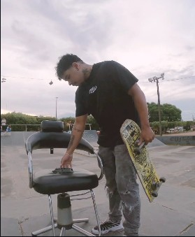 Barbeiro com skate ao lado de uma cadeira de barbearia na pista